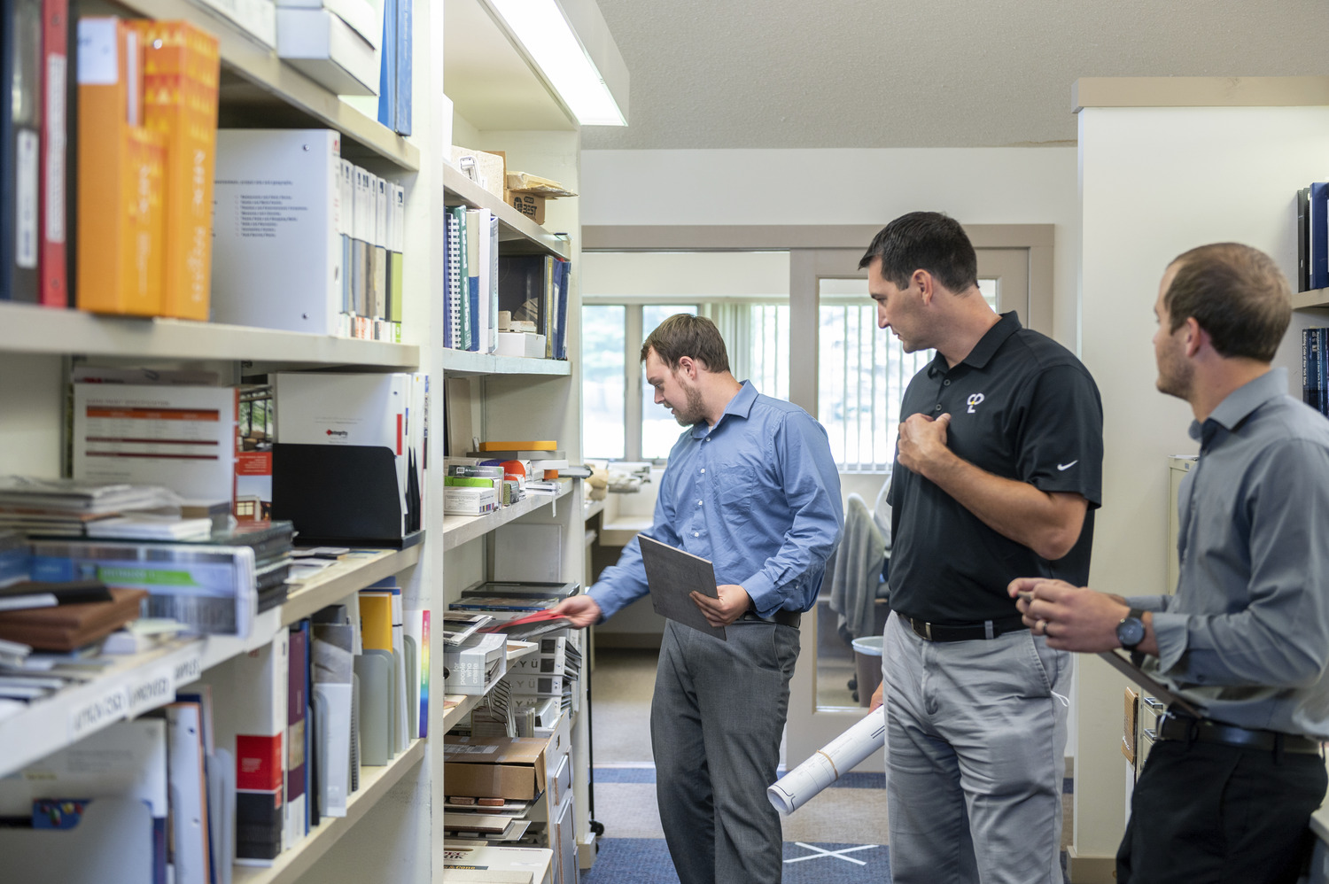 Three men next to a shelf holding binders and books.