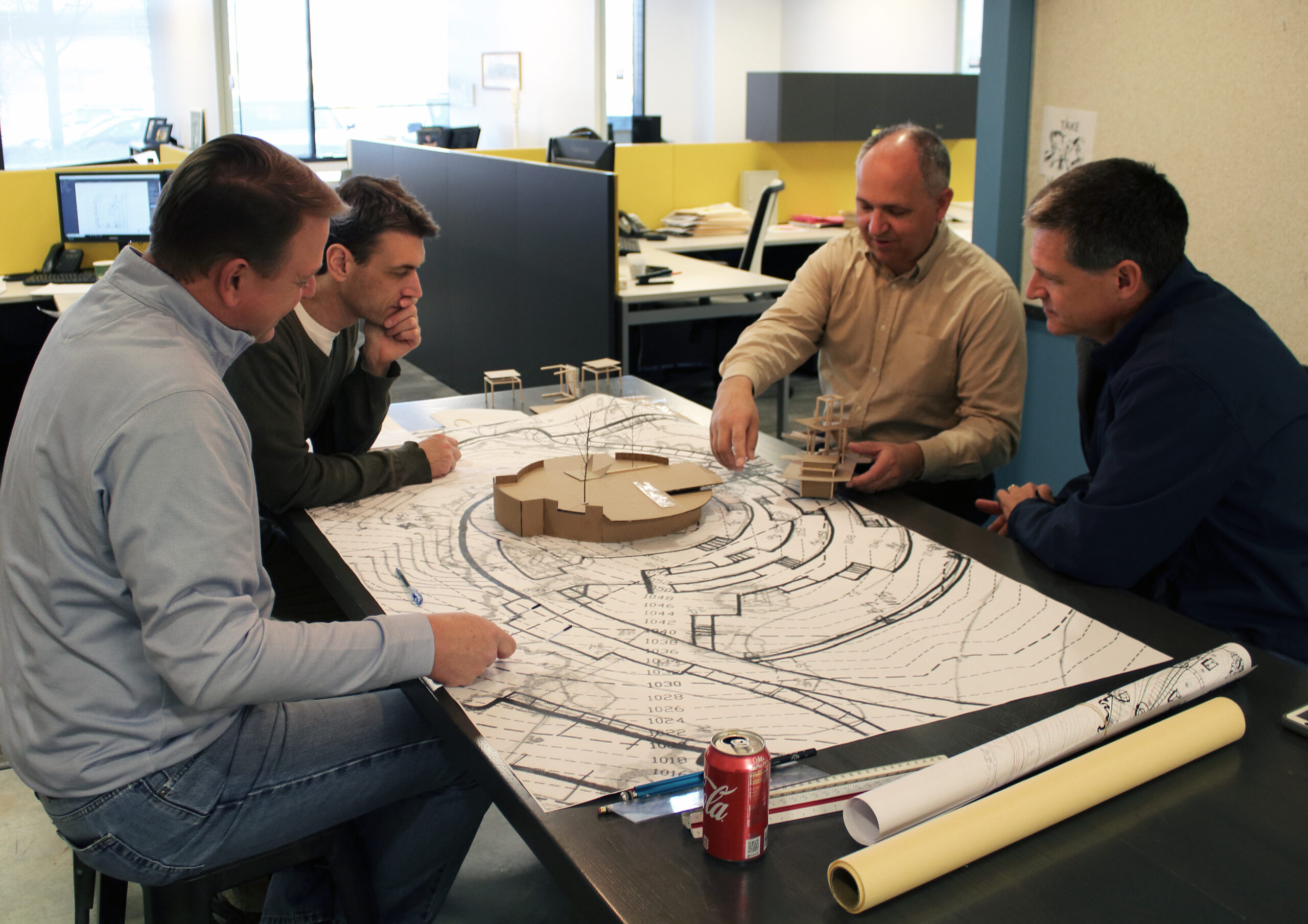 Image shows 4 men sitting around a table and discussing the transportation design architectural plans that are in front of them.