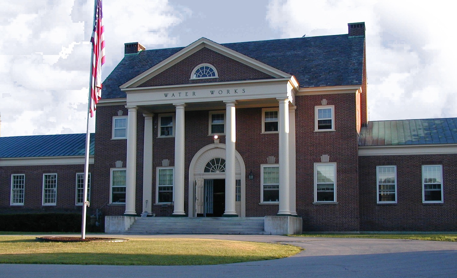 City of Saratoga Springs - WTP Intake Valve. Image shows the City of Saratoga Springs Water Works building. It is a traditional brick building with columns and an American flag out front.