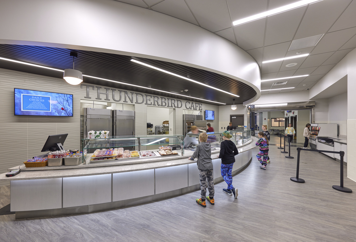 Image shows a cafeteria with a cafe bar. The wall reads "Thunderbirds Cafe" and shows people serving food to students standing in front of the serving station. This is at Chautauqua Lake Central School.