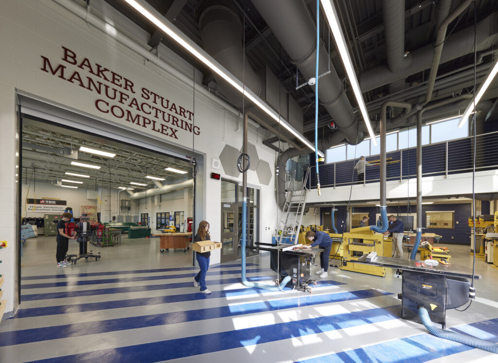 A modern workshop with high ceilings and industrial lighting in the Baker Stuart Manufacturing Complex at Chautauqua Lake CSD. Several people work on projects, creating a busy and productive atmosphere.