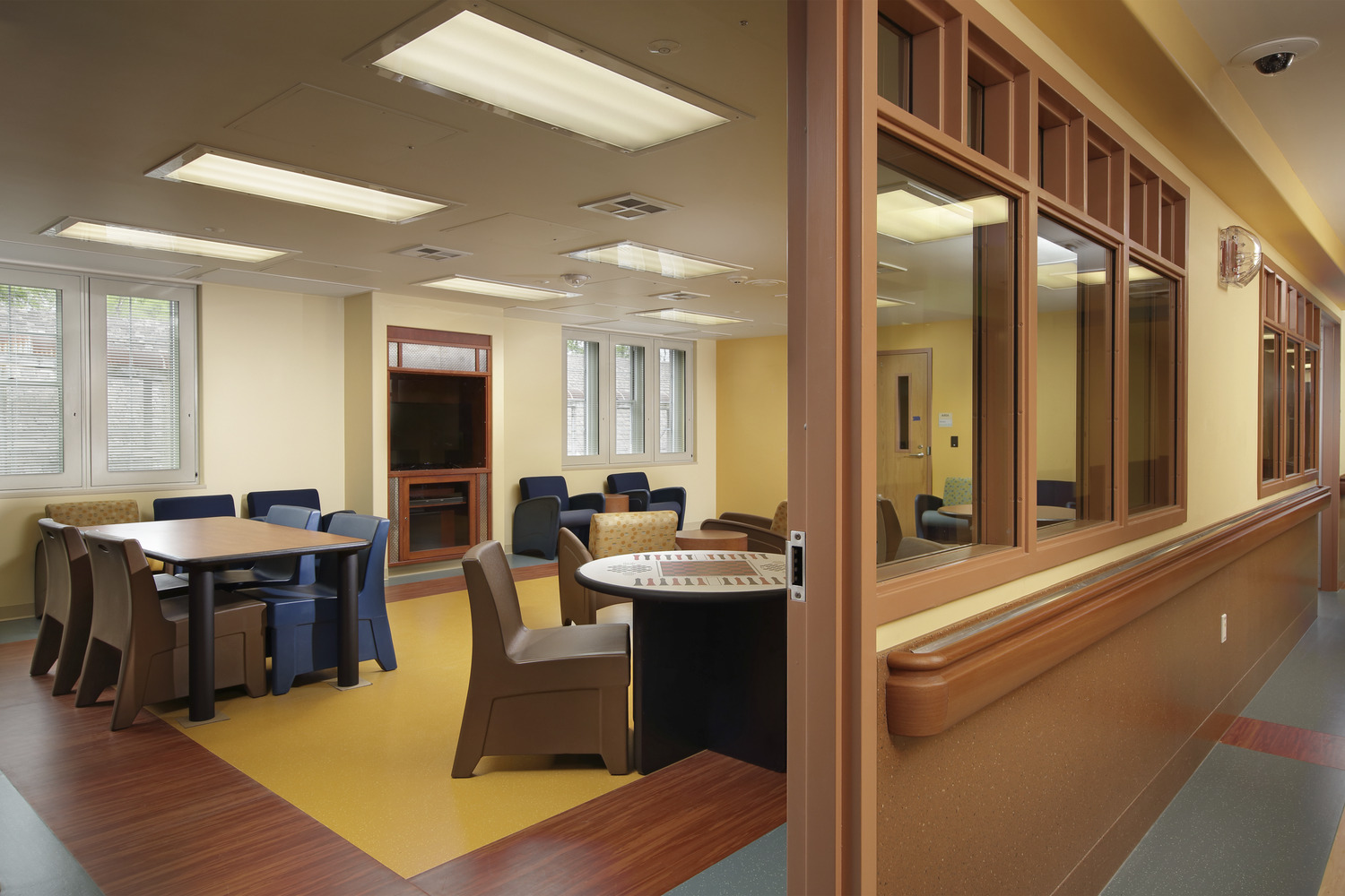 Image shows a lobby at the Children’s Institute Behavioral Health Clinic in Pittsburgh, PA. The room is done in calming tones of yellow, brown, and blue. There are chairs around tables in a lobby setting.