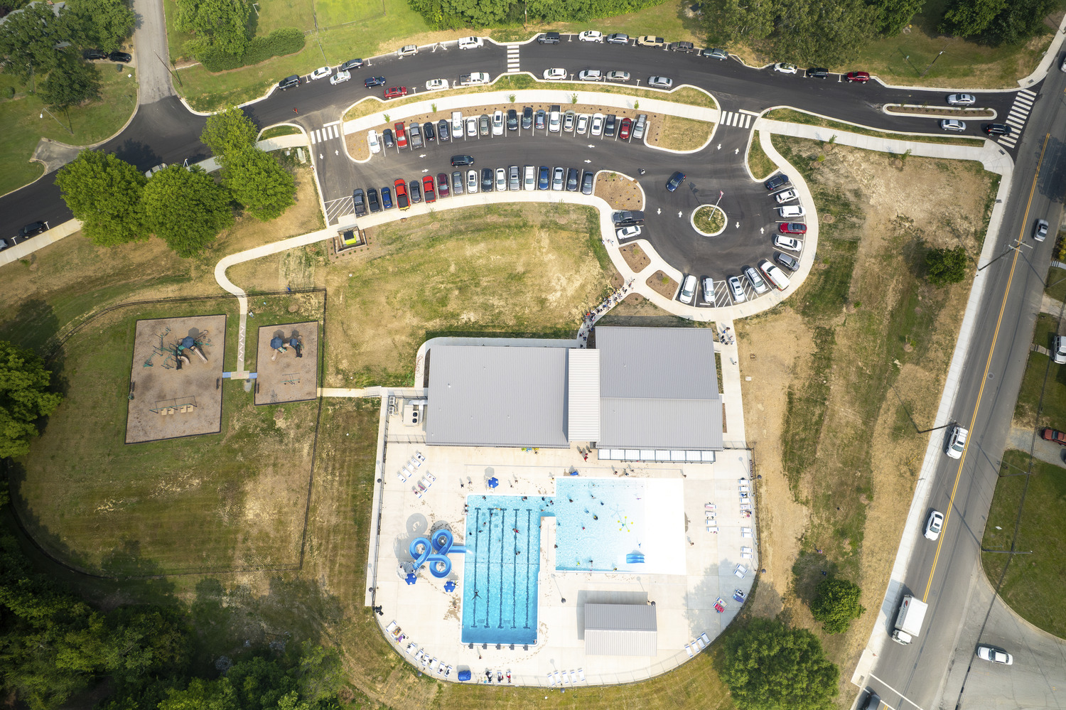 An aerial view of the Thomasville Aquatic and Community Center is shown. Two pools can be seen next to two buildings. There is a parking lot pictured that is full of cars. 