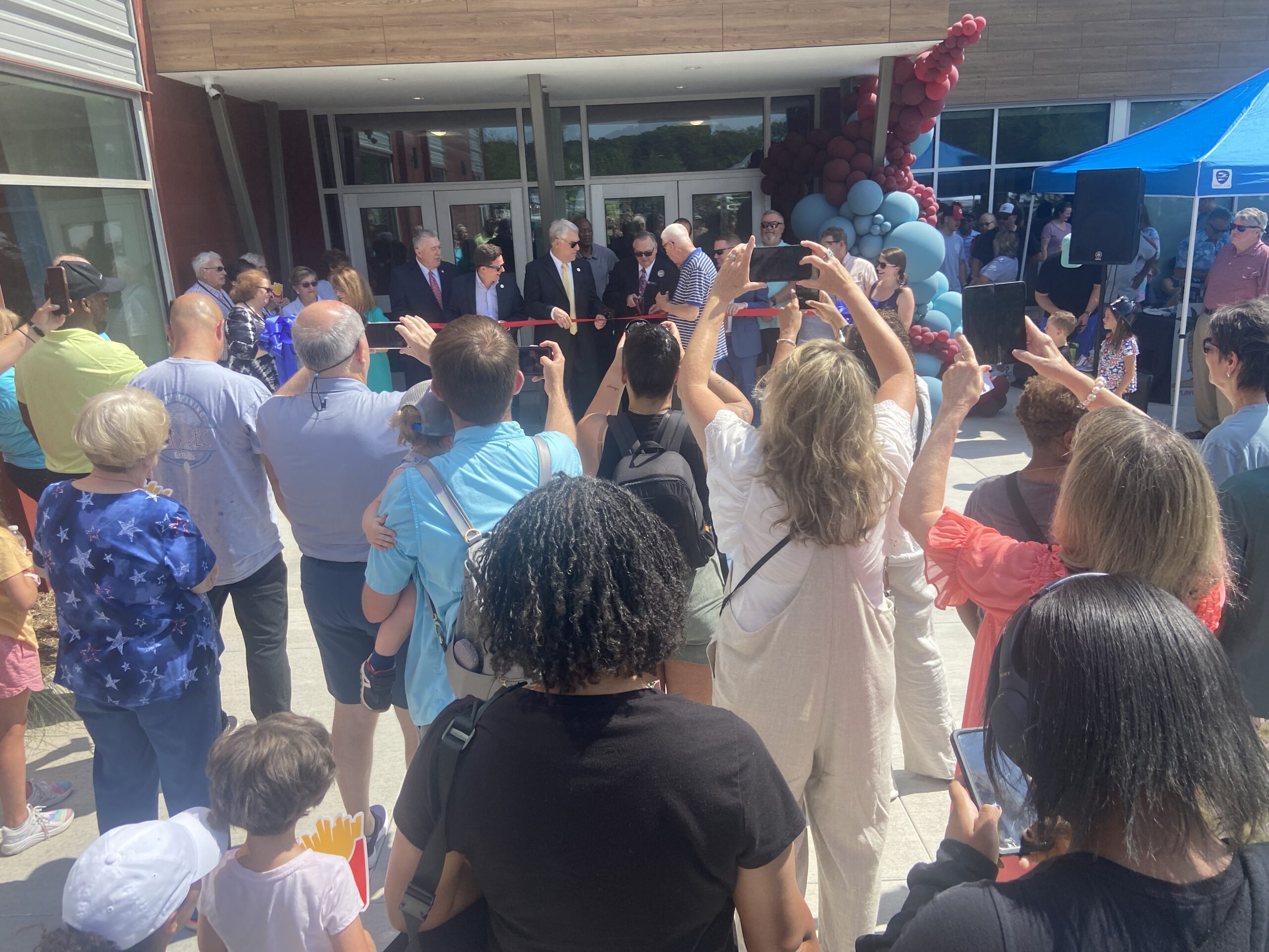 Image shows people in a crowd surrounding the entrance to the CityRec Center in Belmont, NC where there is a ribbon being cut to celebrate the grand opening.