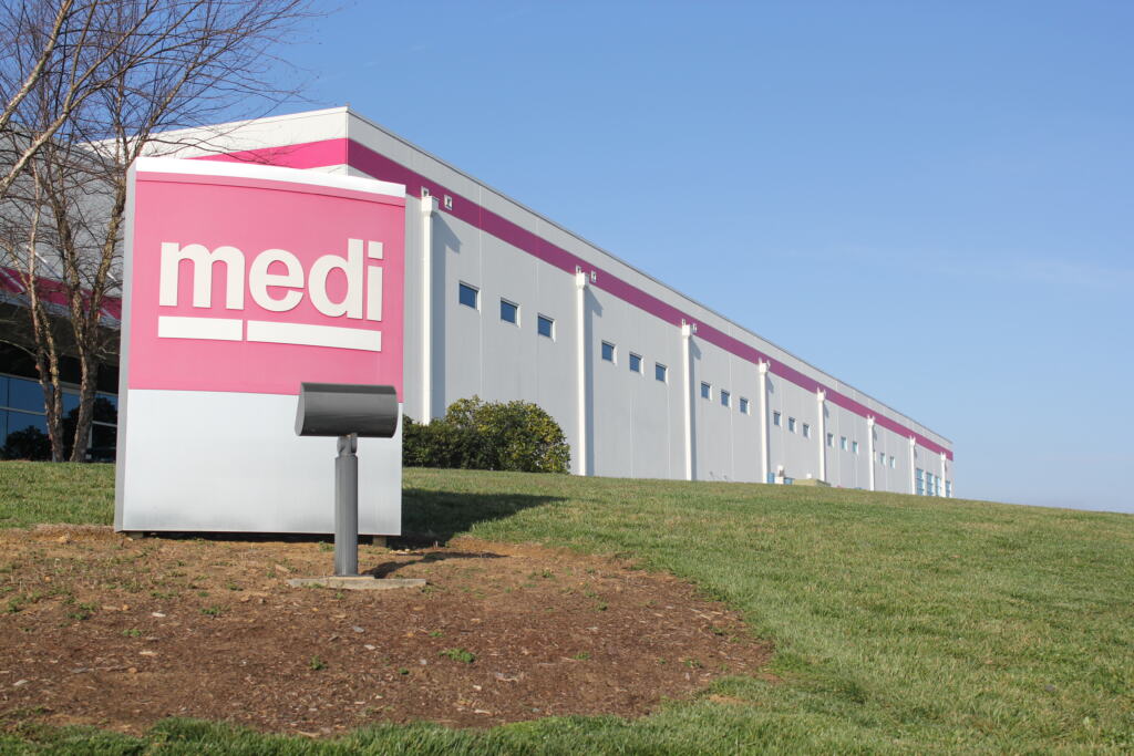 Medi USA exterior. Large white building with magenta accents beneath a clear blue sky. Foreground features a magenta sign reading "medi" on green grass.