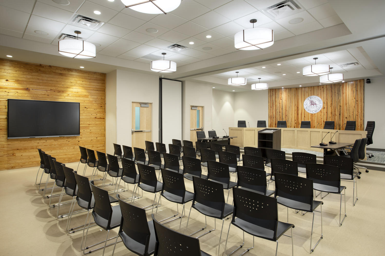 City of Thomasville – Memorial Park Pool & Community Center This is the new City Council Chamber at the Thomasville Aquatics and Community Center. Many chairs in rows are facing a table at the front of the room that has chairs seated at it facing the room. There is a screen on one wall.