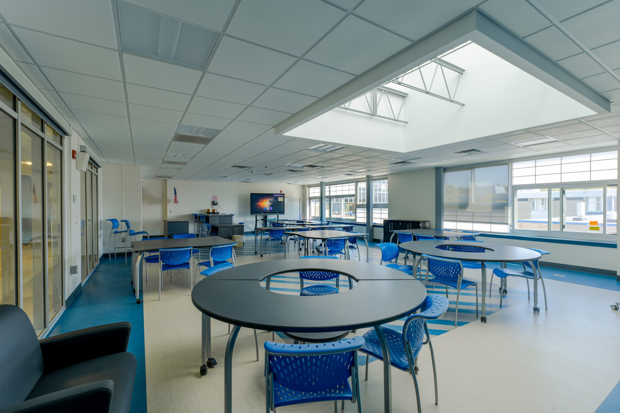 Classroom with round tables with blue chairs, left wall with windows, and skylight