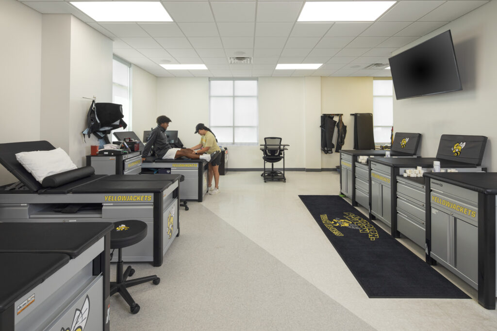 Image shows a room for sports medicine at Duke Hall at Randolph-Macon college. There is a person sitting on one of the medical tables while another person looks at their knee.