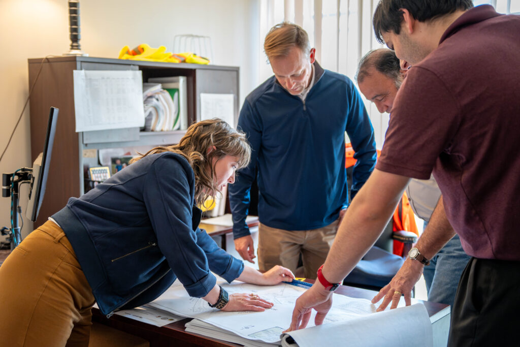 A woman and several men work on plans and municipal zoning codes together, huddled around a desk