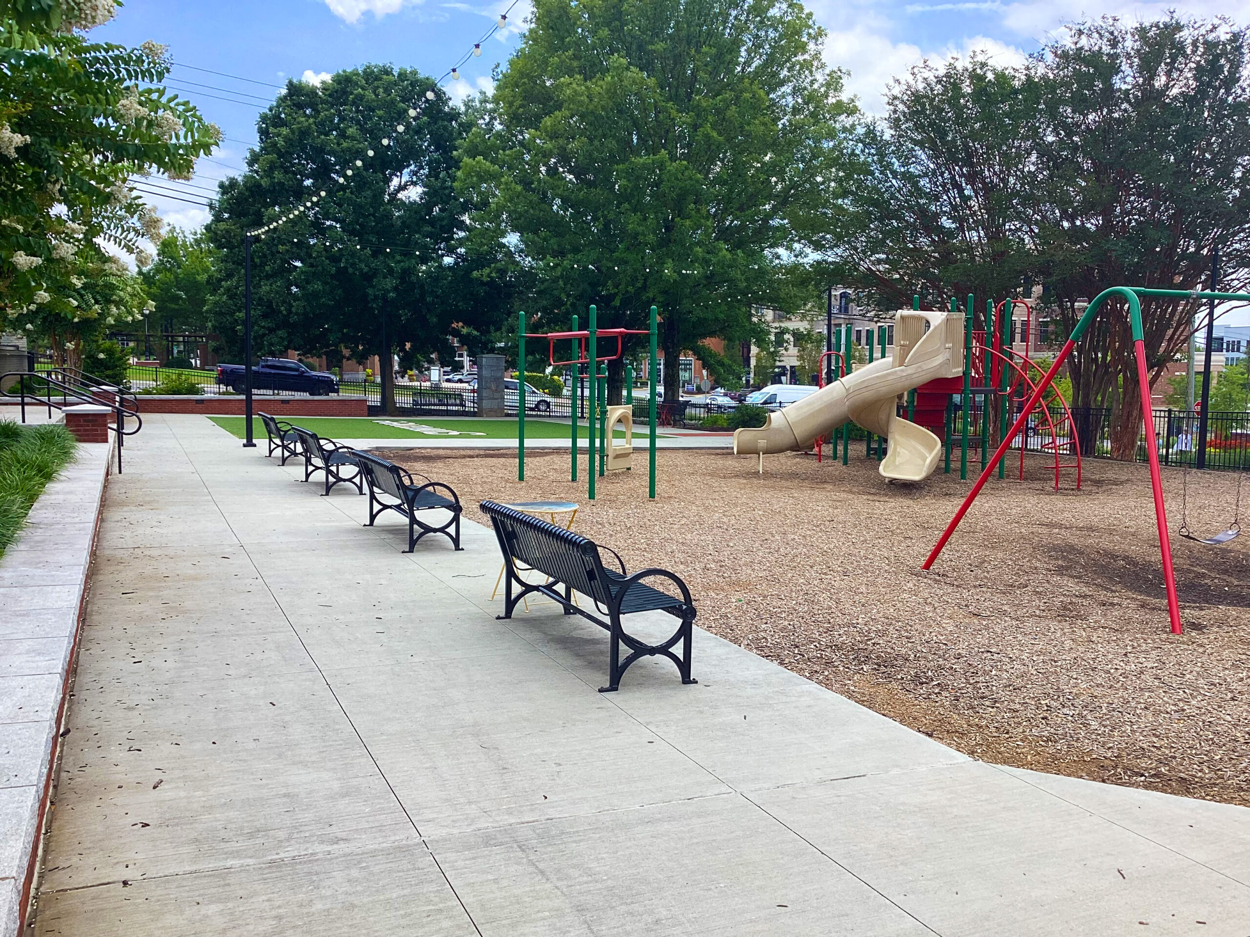 A playground with a sidewalk around it and benches on the sidewalk at the Suwanee Station Park