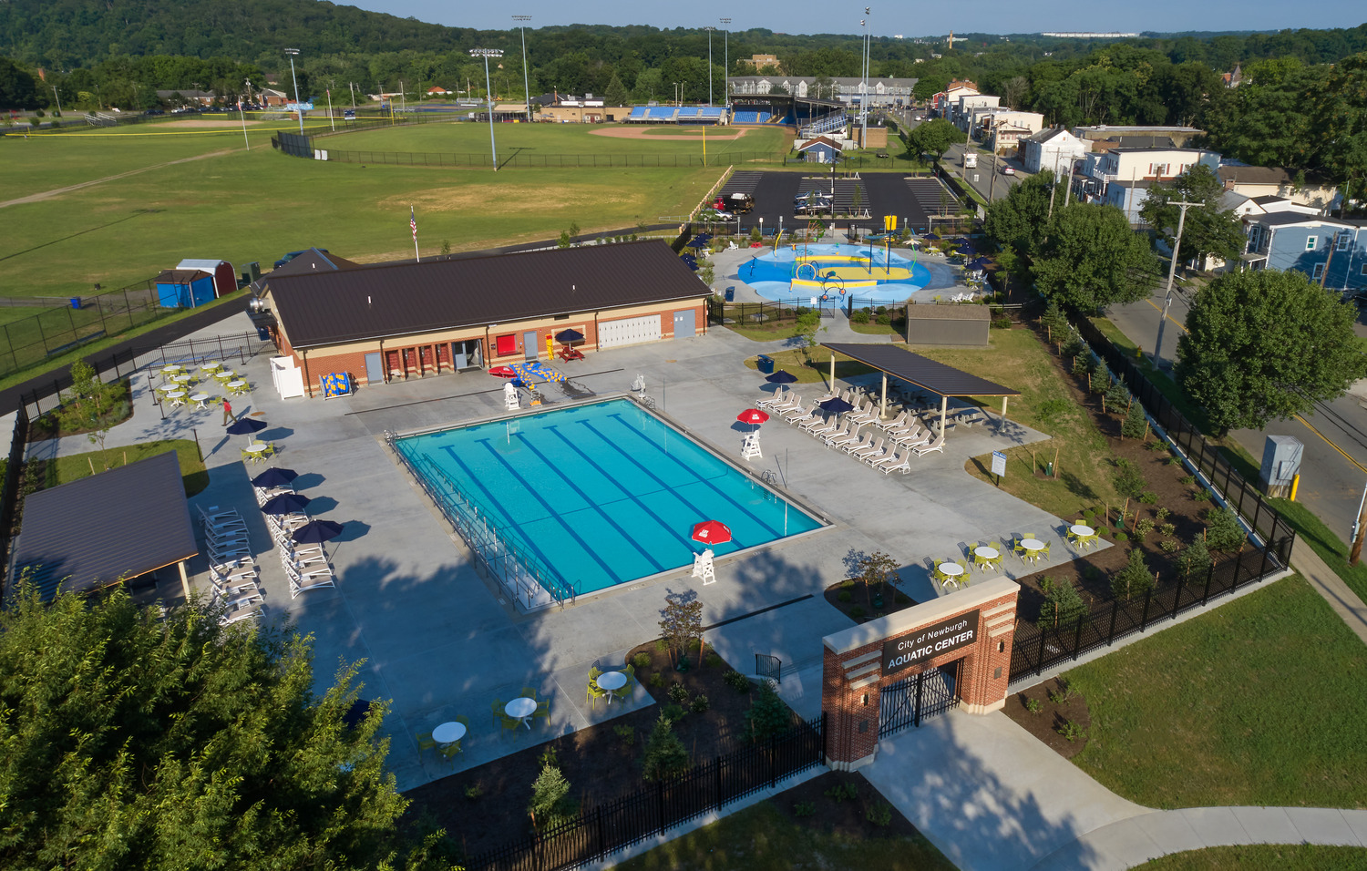 An aerial view of the Delano-Hitch Aquatic Center with Pool and Splash Park. A baseball field can be seen in the background. There is a sign at the entrance of the park that reads "City of Newburgh Aquatic Center"