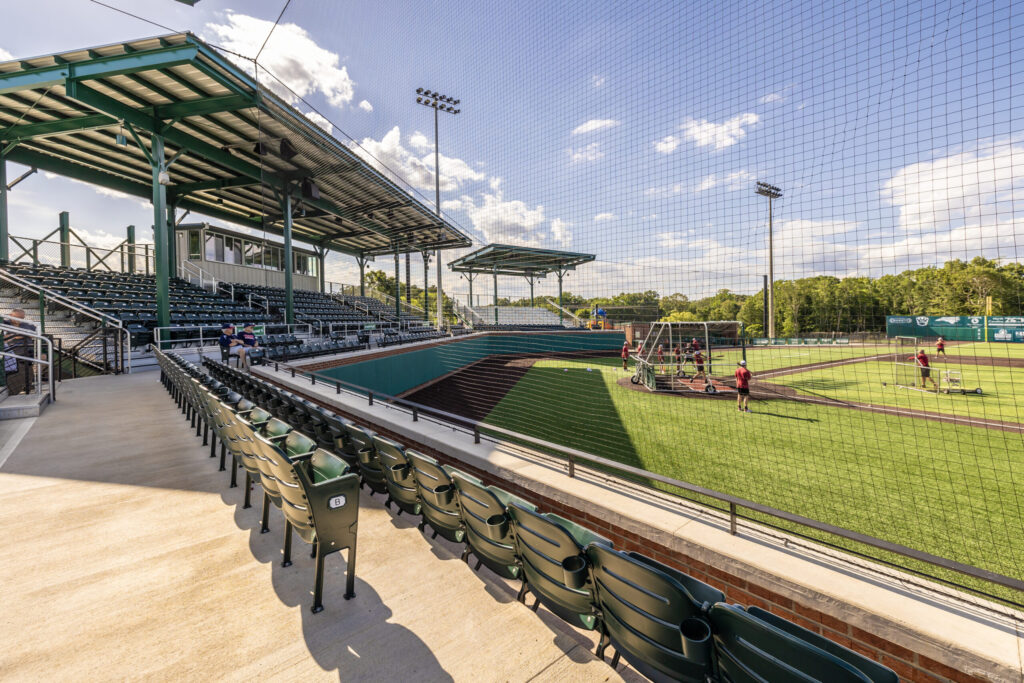 Baseball field patio, seats and bleachers with players practicing,