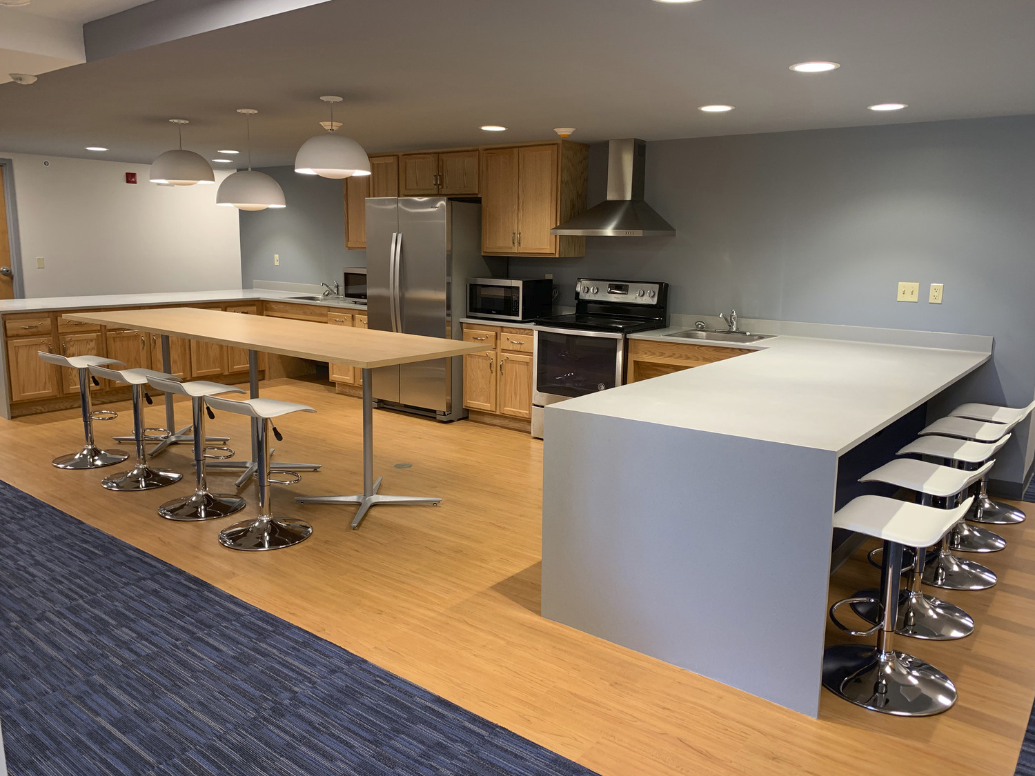 A modern kitchen with bar seating, contemporary light fixtures and brown cabinetry.