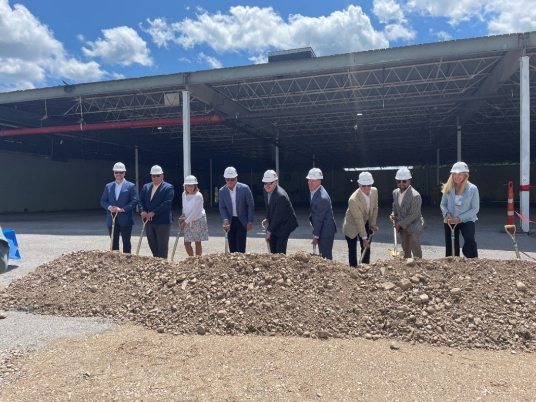 A group of people holding shovels to break ground on a new construction project, with a clear blue sky in the background.