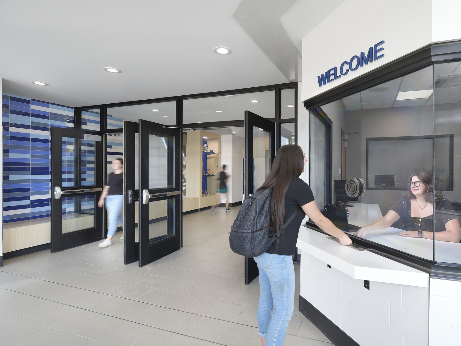 A student chats with an administrative faculty member at the welcome/reception area of a high school.