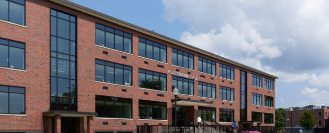 the exterior of Plassmann Hall, a brick building with many windows, on a bright and sunny day.