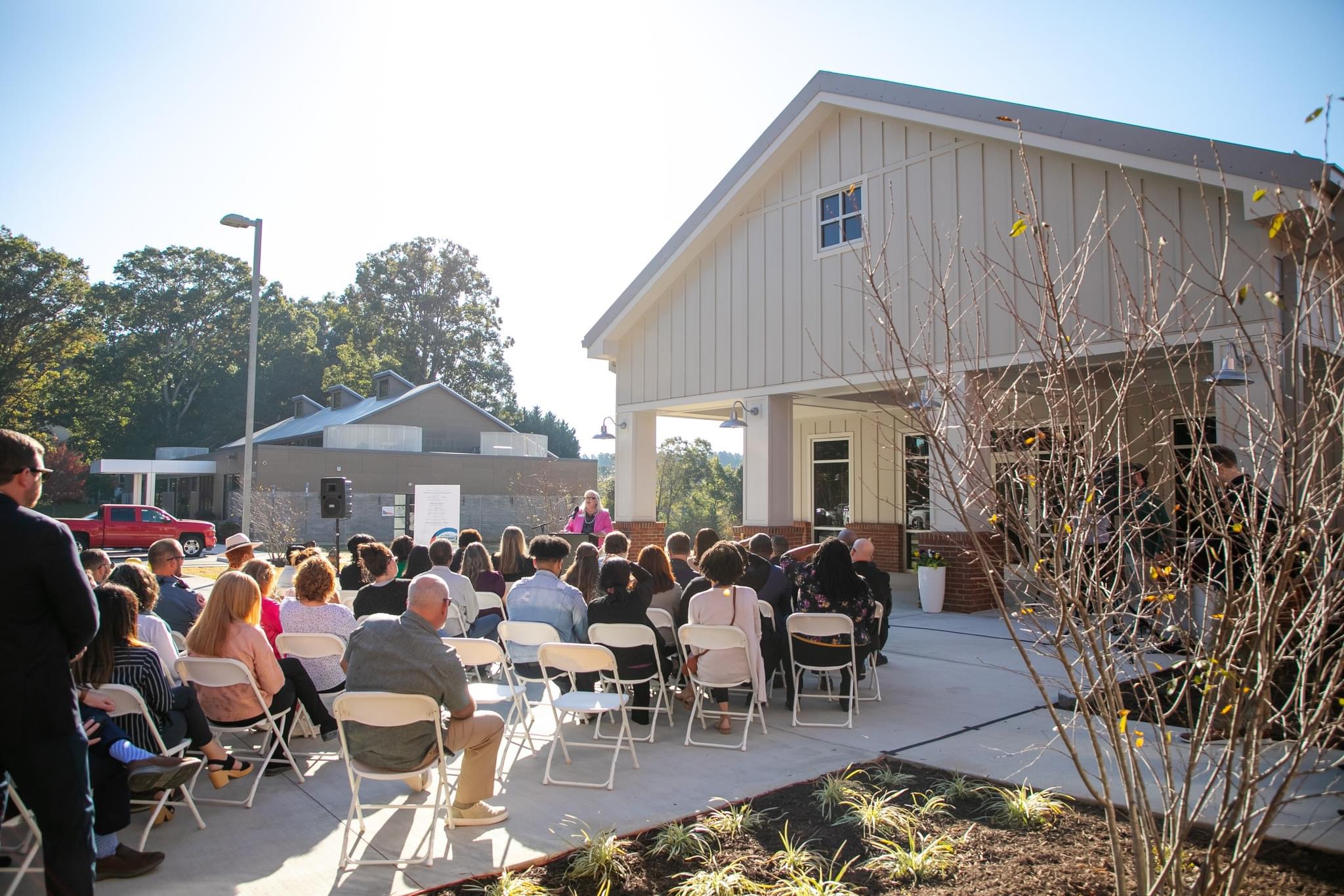 A group of people sitting outside a new community destination health and education center, commemorating its official ribbon-cutting on a sunny day.