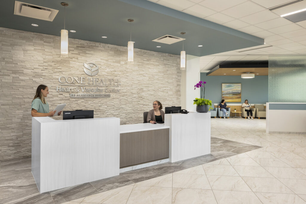A front reception desk at a cardiac care facility, with two staff members standing in front of a warm ledgestone wall.