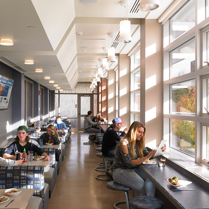 State University of New York at Geneseo Letchworth Dining Hall. Modern café with large windows and natural light. People sitting at tables, enjoying food and conversations in a relaxed, inviting atmosphere.