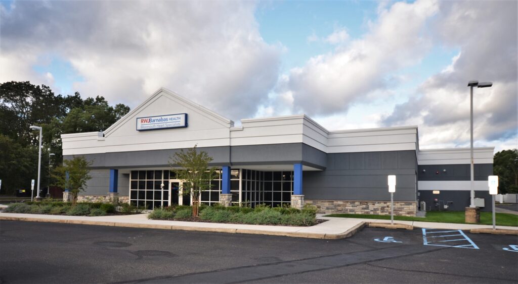 An exterior image of the entrance to the health center, with shrubs, grass, and a blue sky.