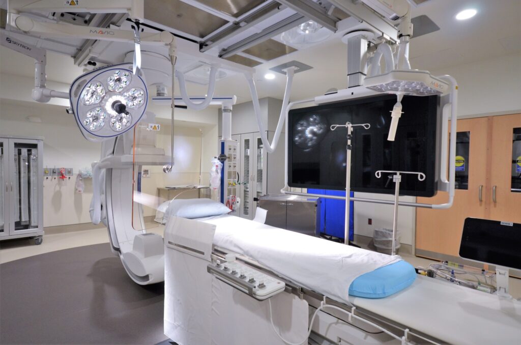 Inside the Community Medical Center lab, a table for the patient is surrounded by modern medical equipment and a large screen is on the far wall.
