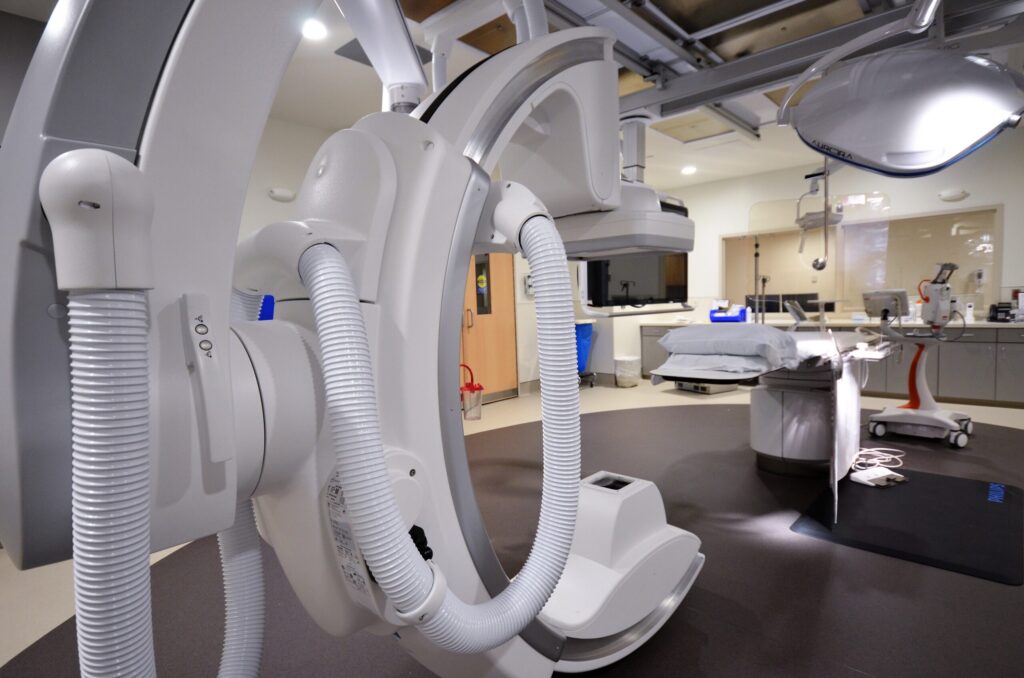 A close-up shot of the ceiling-mounted C-arm imaging machine, with the rest of the lab in the background.