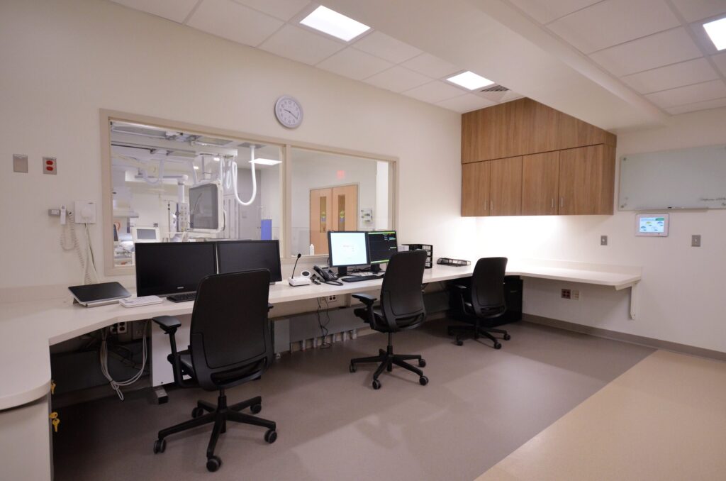A view of an observation room with cabinets, a desk, chairs, and a window overlooking the lab.