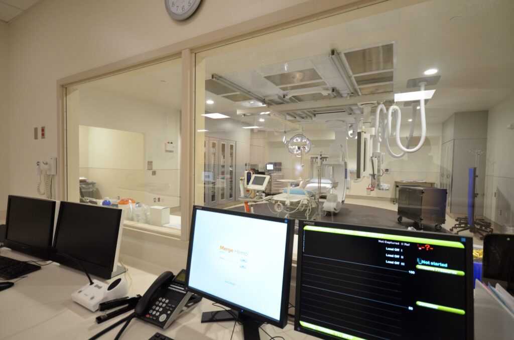 Monitors on a desk in front of an interior window, overlooking the Community Medical Center lab.