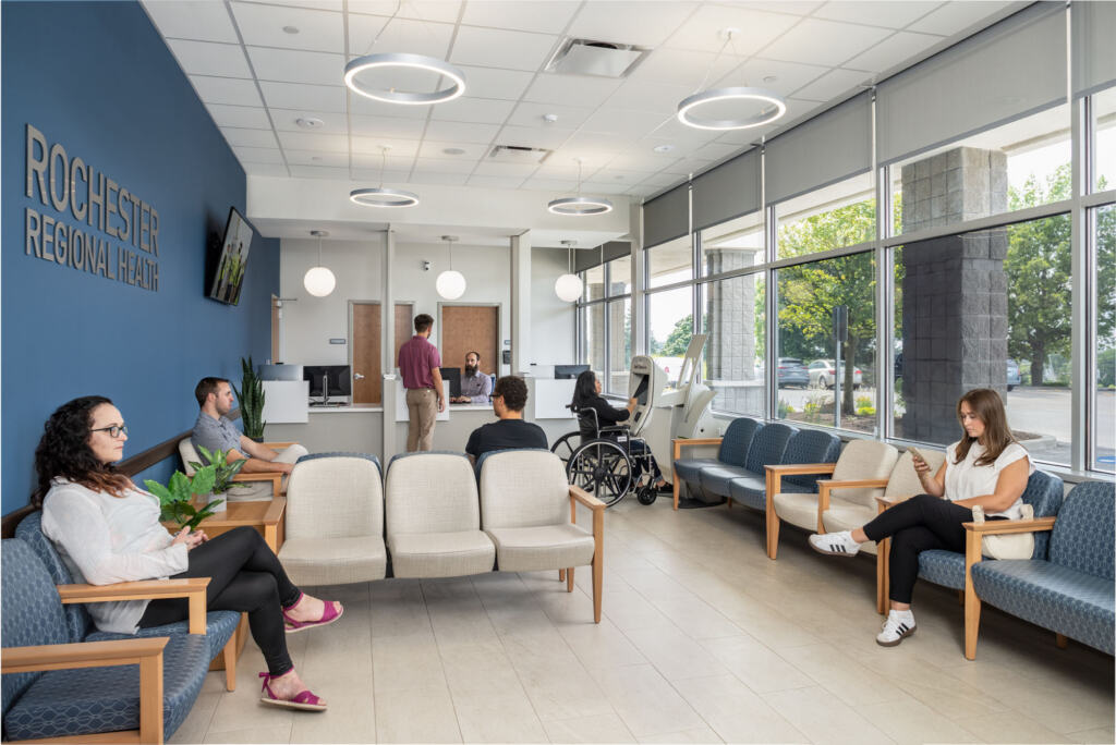 Waiting room with blue wall with a television on it and people checking in at Victor Medical Campus