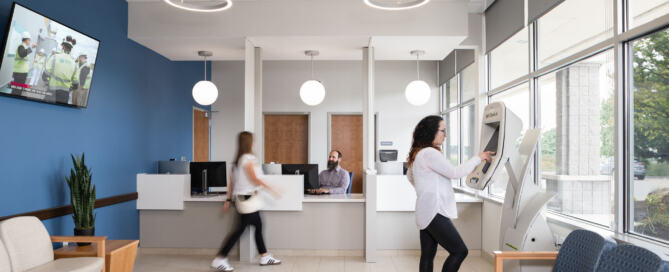 Waiting room with blue wall with a television on it and people checking in at Victor Medical Campus