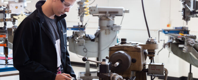 A K-12 student operates machinery in a high school STEM workshop / classroom.