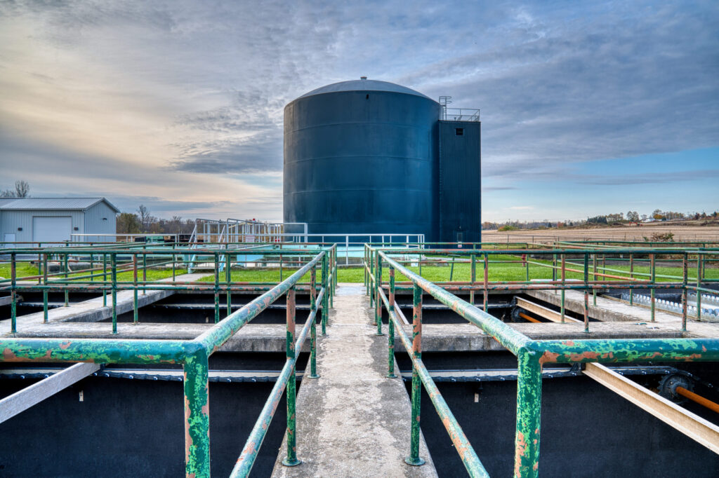 Metal walkways in the foreground, and one water tank of the wastewater treatment plant centered in the distance.