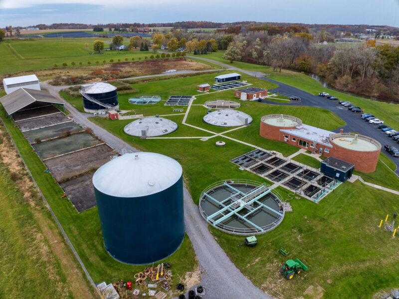 An aerial view of the Lakeville wastewater treatment plant, in a green field with forests and a skyline in the background.