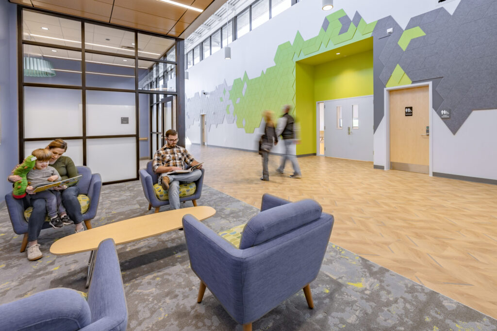A few people sitting in a breakaway space in a large hall with fun wall decor, reading.