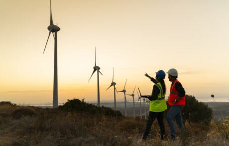 Silhouette of young engineer holding laptop computer planning and working for the energy industry and standing beside a wind turbines farm power station at sunset time