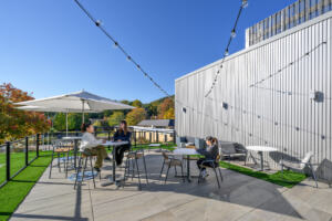 Students studying outside at a table on a patio, next to an academic building, with a blue sky in the background.