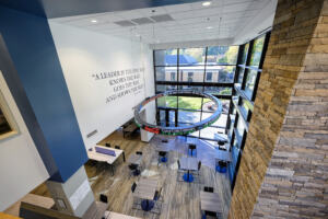 A view from above of the interior lobby of the business building, groups of tables and chairs, a circular lighting element, a quote on the high wall, and natural light coming in.