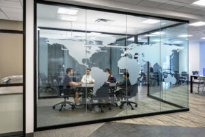 Students meeting at a long table in a breakaway space, which is behind a glass divider sandblasted with a world map silhouette.