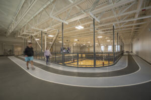 Two people in athletic wear walking an indoor track that wraps the perimeter of basketball courts.