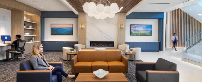 People resting and working in a sitting area with cushy chairs, a sofa, coffee tables, unique overhead lighting and artwork on the far walls.