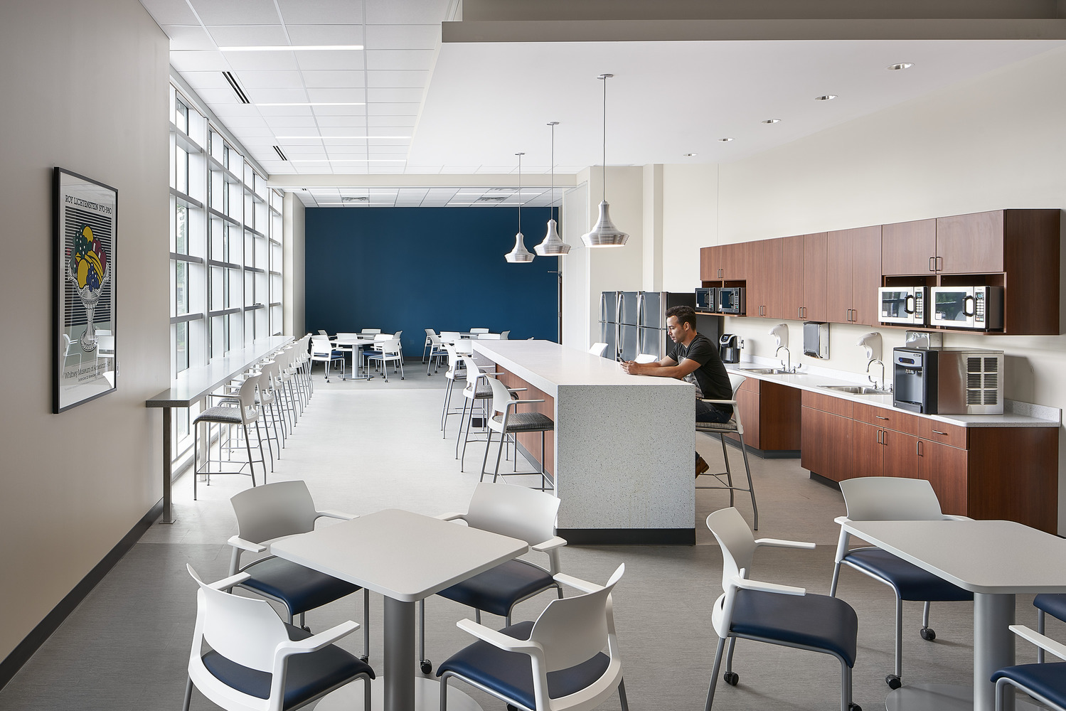 A break room space with tables and chairs. On one wall are cabinets with microwaves and sinks. A person is sitting at a table at Rochester Regional Riedman Health Center.