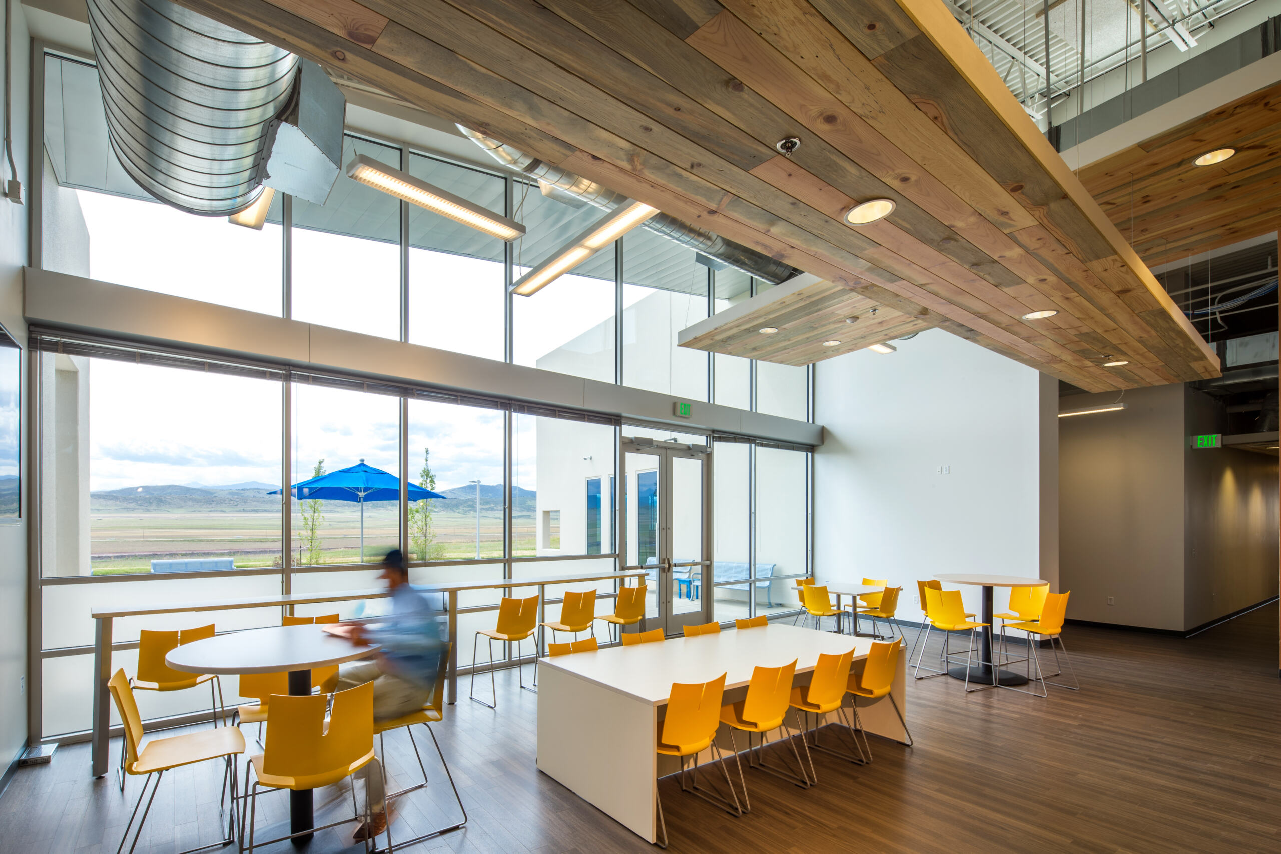 CP_2015_002_Nordson_Value_Plastics_Colorad_N75 copy Employee eating lunch next to large windows in kitchen space with yellow chairs and wood floors and ceilings at Nordson Value Plastics