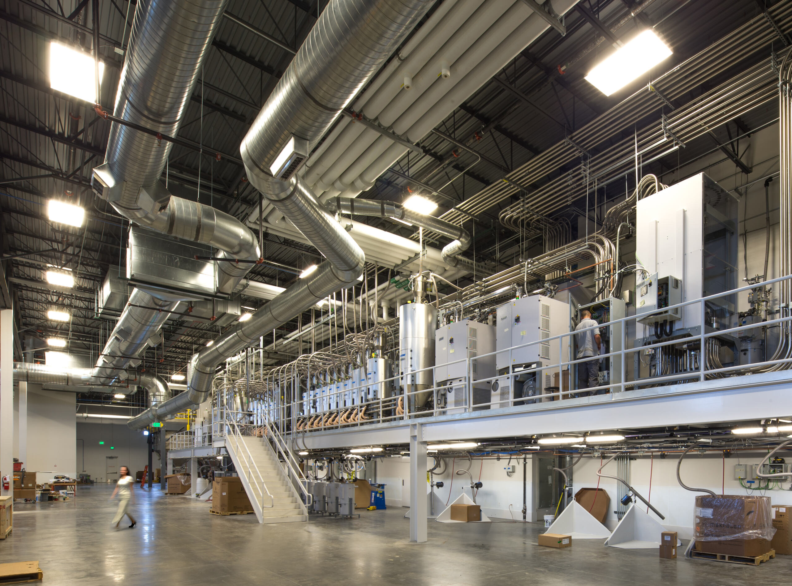 CP_2015_002_Nordson_Value_Plastics_Colorad_N89 copy Interior of a modern industrial facility featuring extensive HVAC ductwork, elevated machinery platforms, and complex piping systems at Nordson Value Plastics in Colorado.
