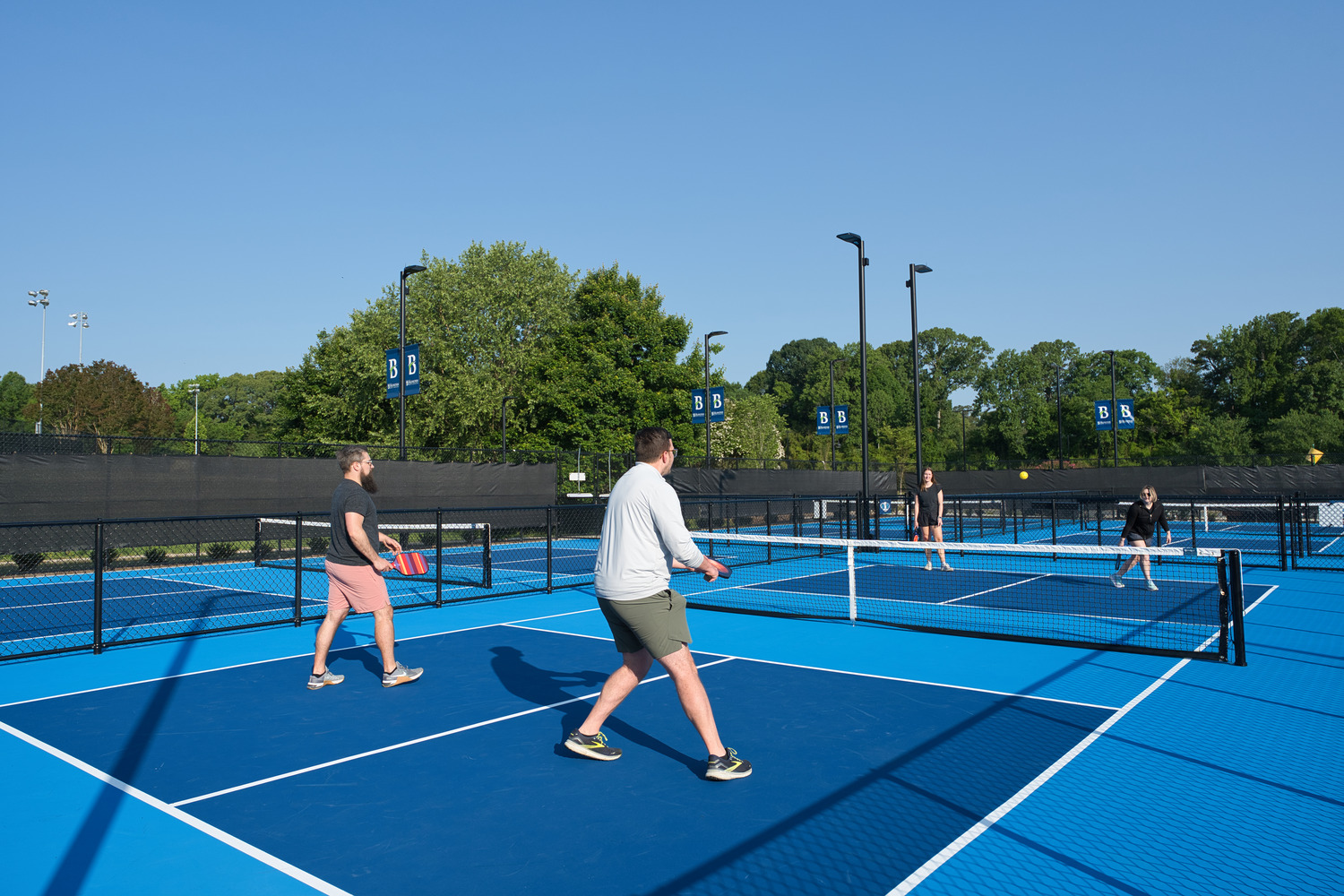 A team of two play pickleball against another team, on a clear and sunny day.