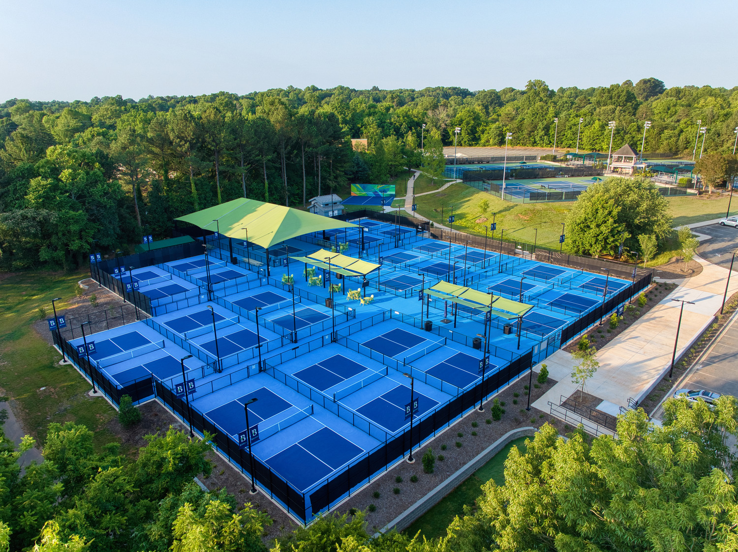 Drone view of the Burlington pickeball complex, with several blue courts, surrounded by forest and fields.