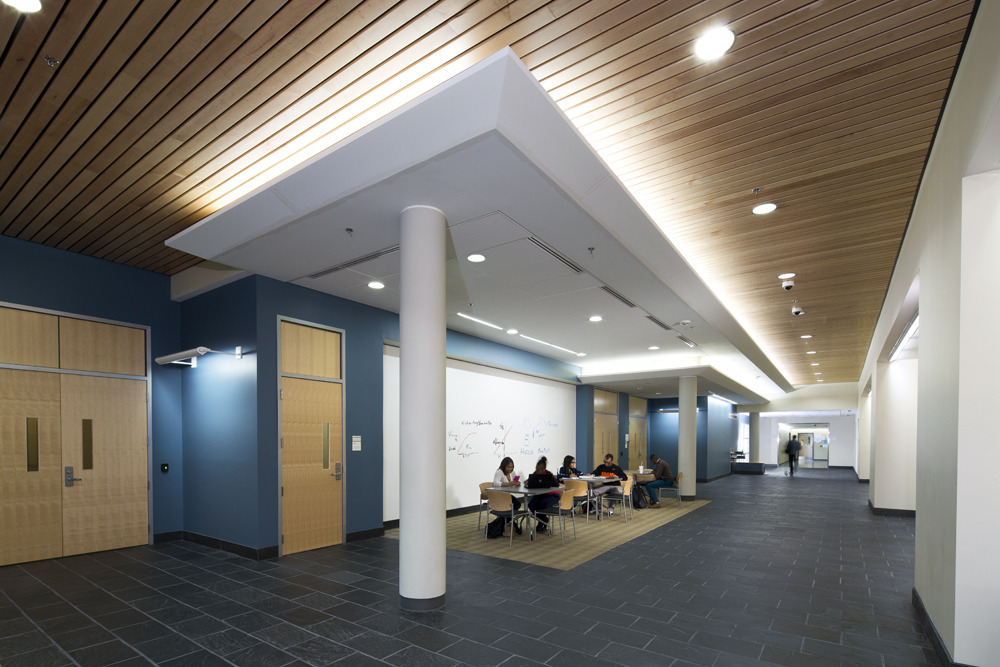 CMW_2015_002_N29_medium Wood paneled ceilings, bright lighting and a breakaway space with furniture and students studying in a wide hallway.