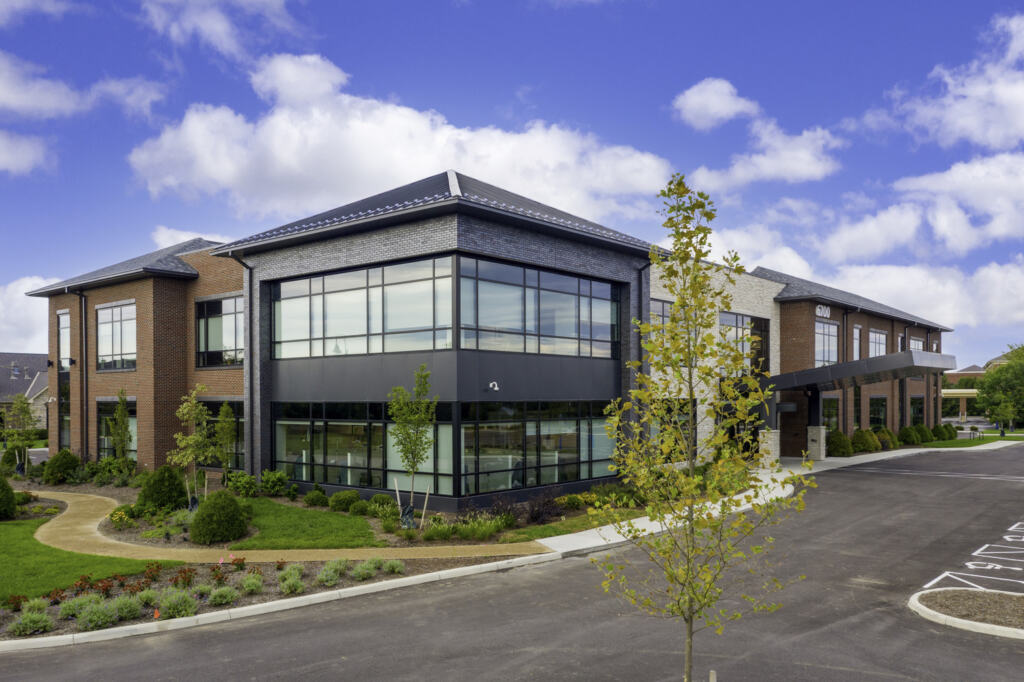 Dublin Cancer Center Exterior showing a modern two-story brick and glass building with large windows on a sunny day. Features a landscaped garden and clear blue sky with fluffy clouds.