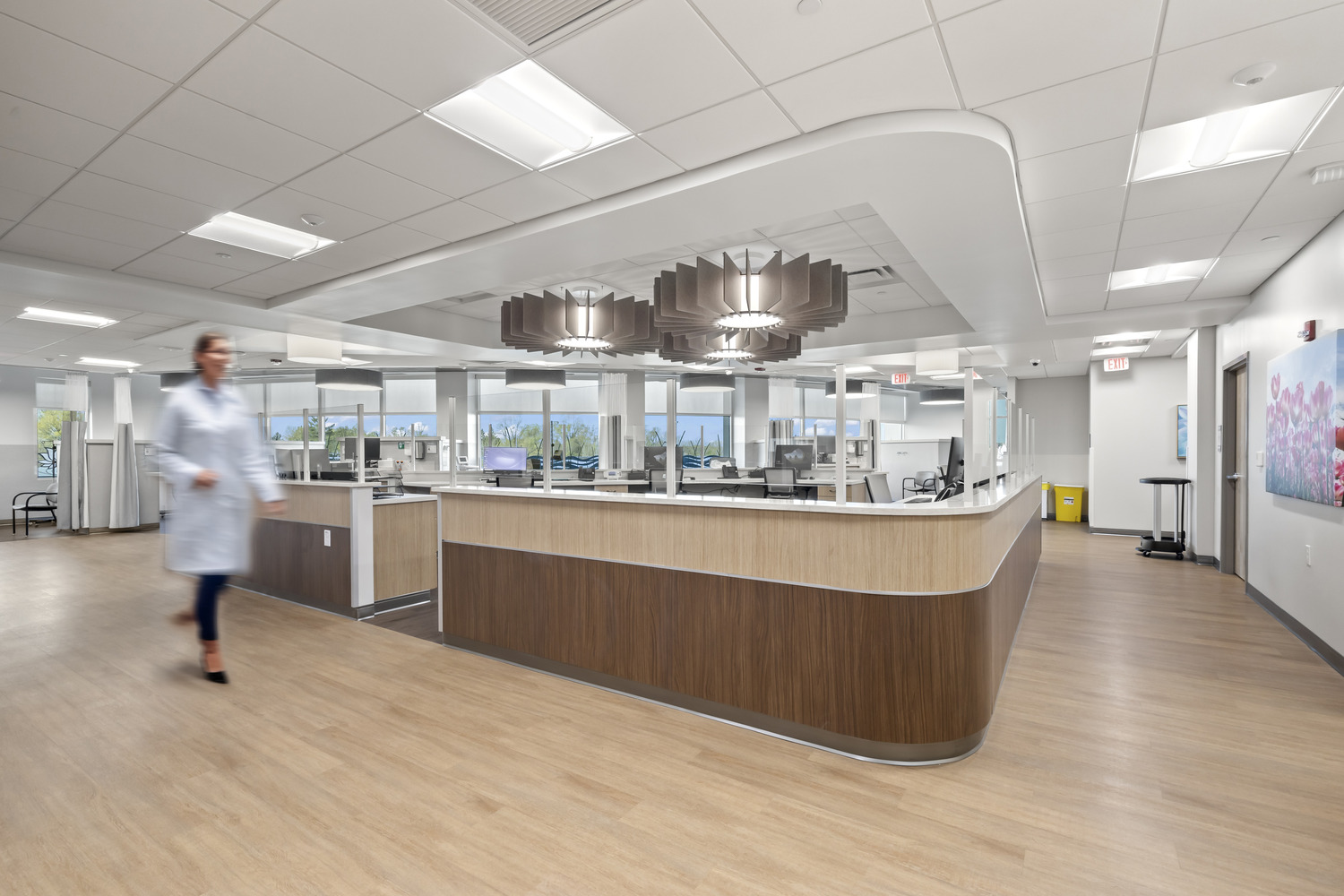 A doctor walks past a decentralized nurse station inside4 Westerville Cancer Center, in a brightly lit area with floral decorations.