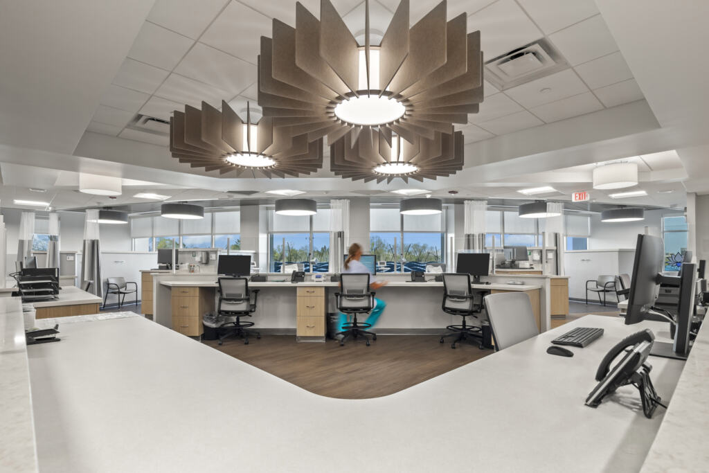 A nurse's station at Westerville Cancer Center has a counter with multiple desks and unique overhead lighting. A woman sits at one of the monitors and types.