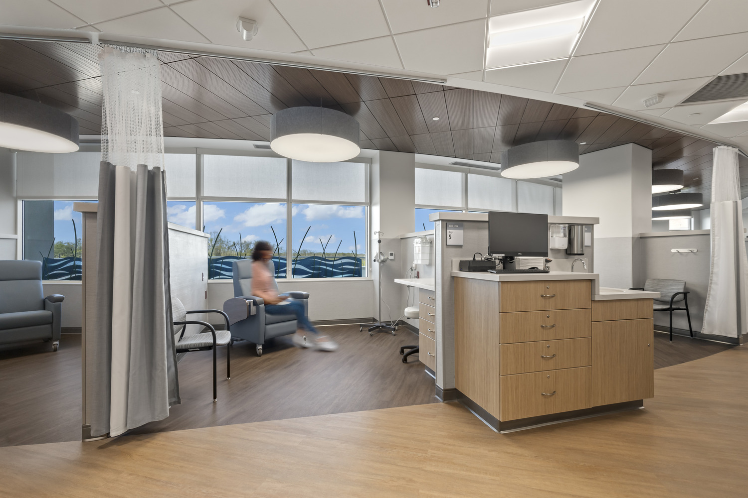 A patient in a salmon shirt sits in one of many Westerville Cancer Center medical bays against a calming window backdrop.